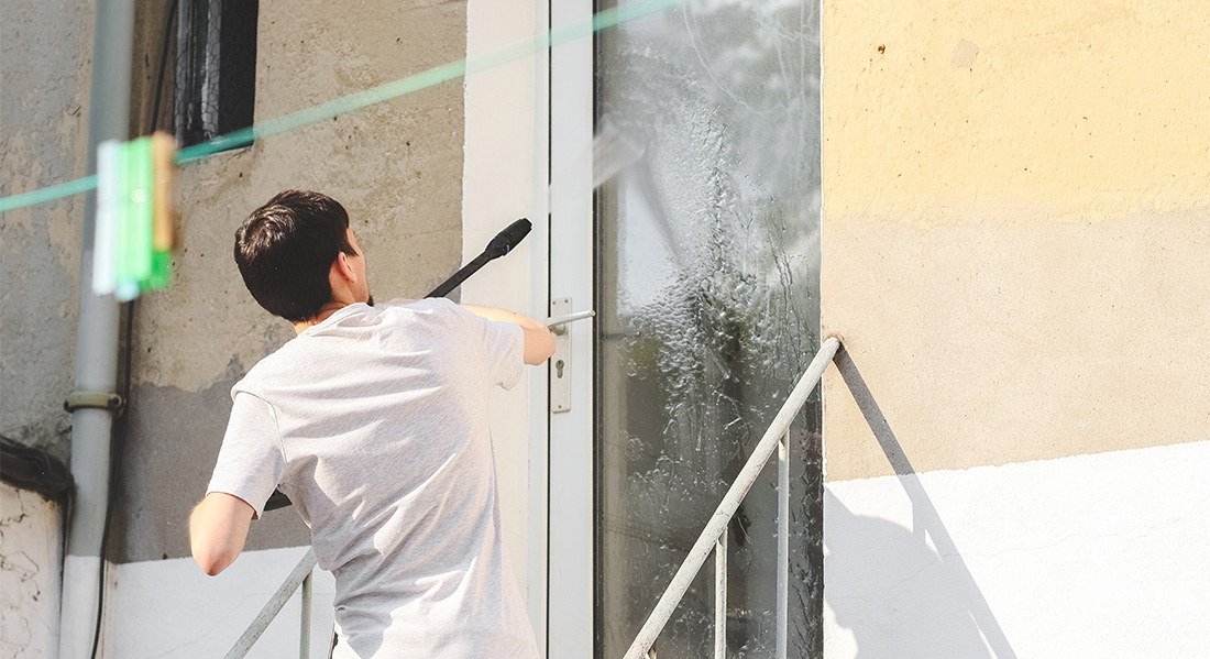 person pressure washing glass on door